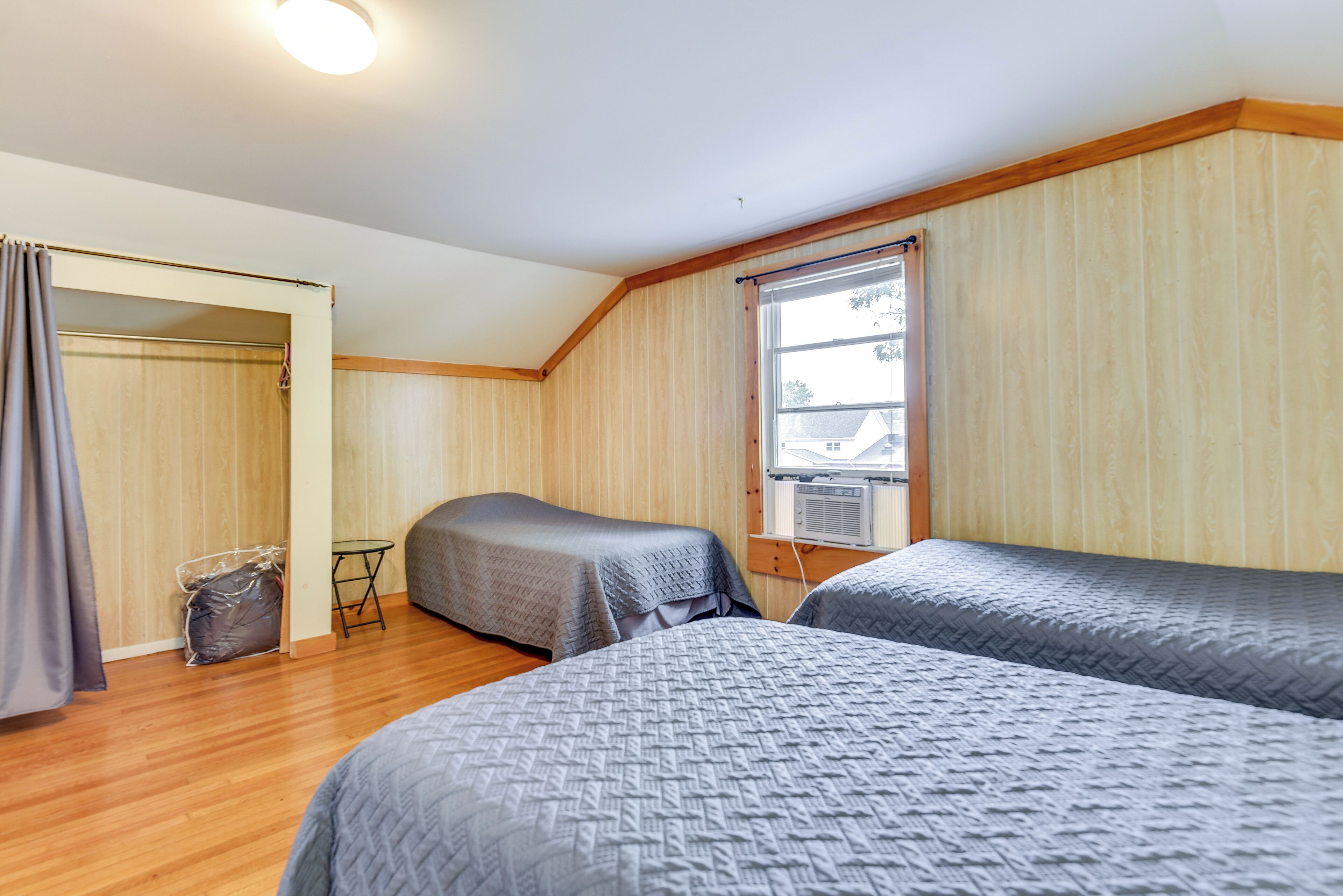A room with two beds, wooden flooring, a window with curtains, and a ceiling light.