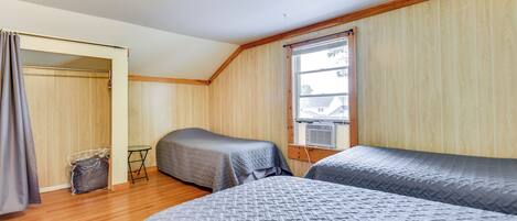 A room with two beds, wooden flooring, a window with curtains, and a ceiling light.