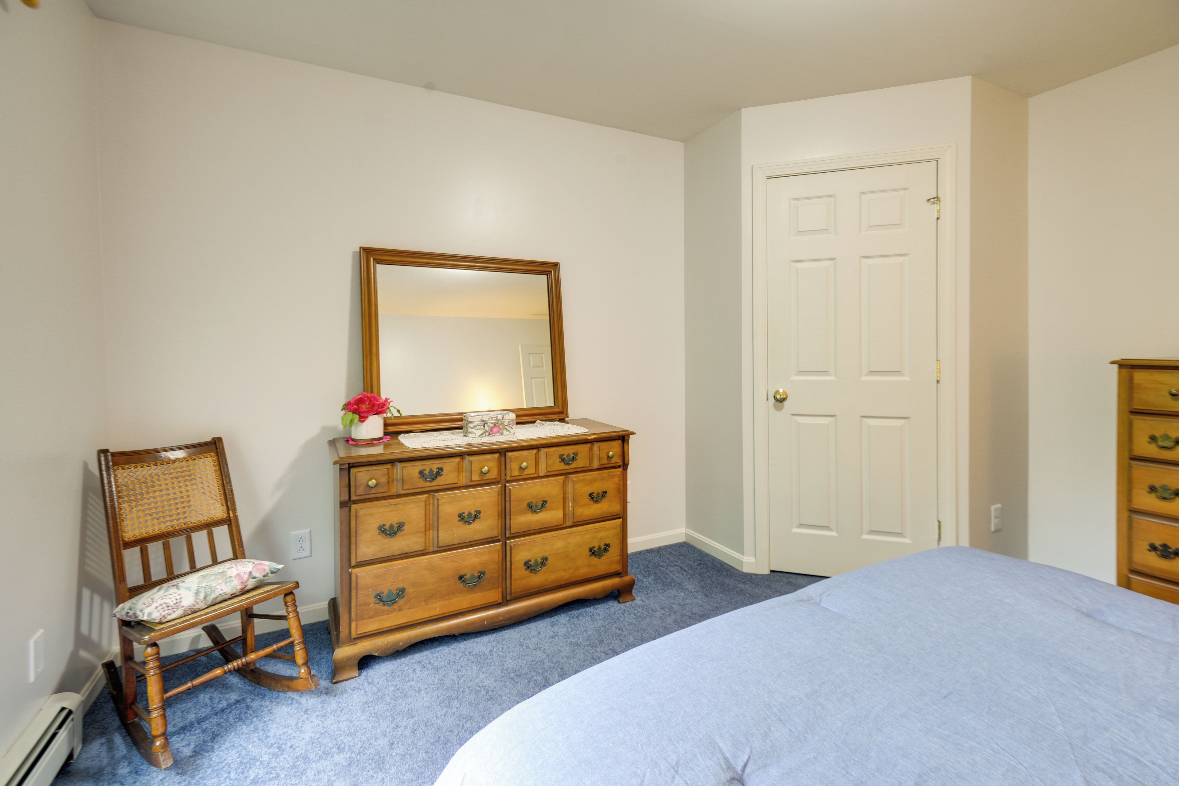 Een slaapkamer met een bed, een kaptafel met spiegel, een stoel en een deur.