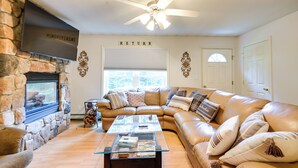 A living room with a stone fireplace, a large leather sectional sofa, a glass coffee table, and a ceiling fan. - Cozy Campton Home: 10 Mi to Tenney Mountain Resort (Campton)
