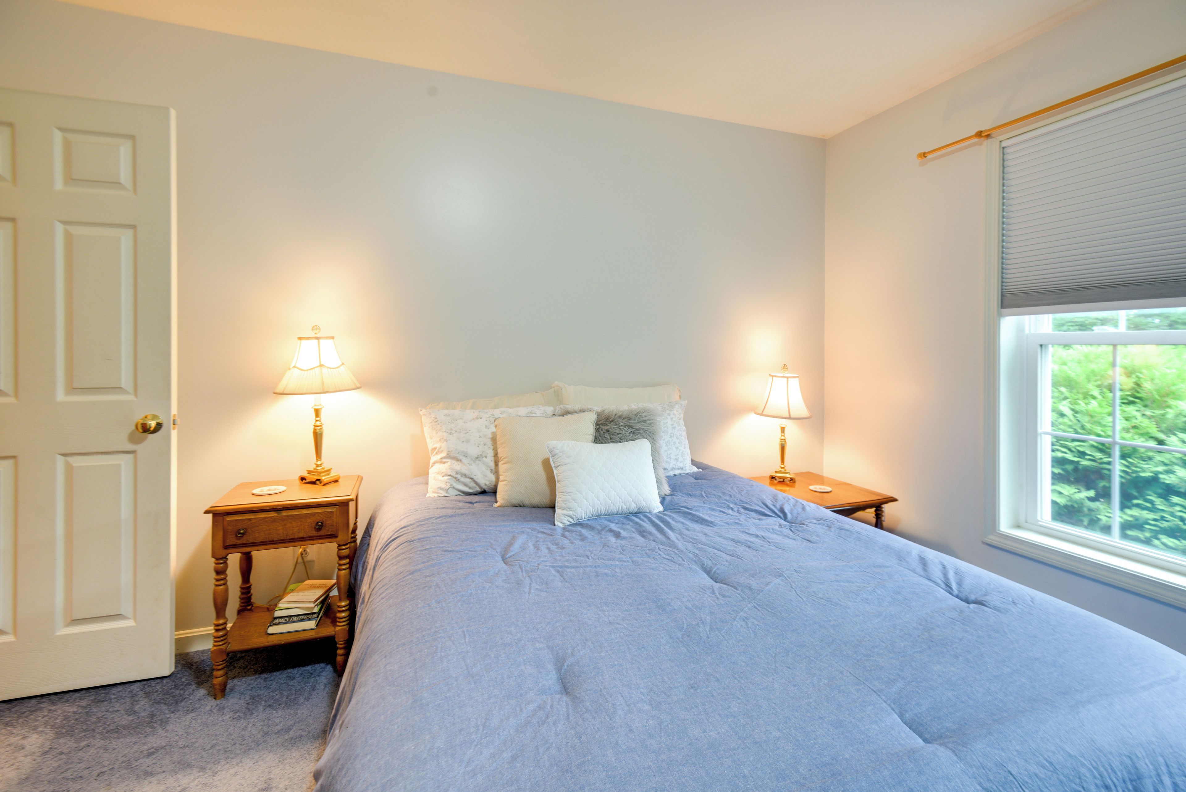 A bedroom with a bed, two bedside tables with lamps, a door, and a window with blinds.