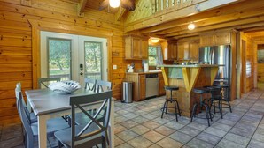Een houten chalet met een keukenhoek, inclusief een eettafel, stoelen, een koelkast en barstoelen.