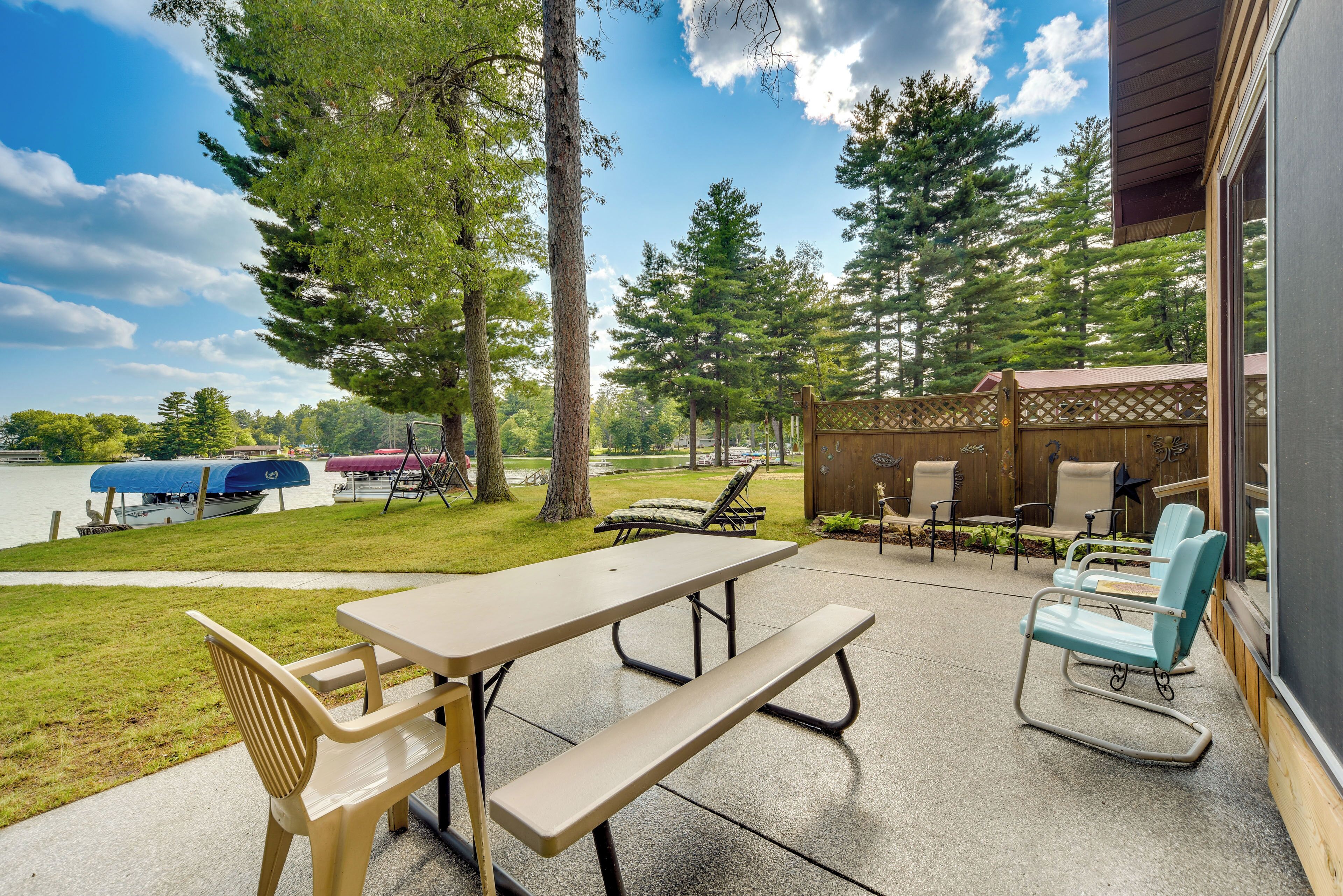 An outdoor patio with a picnic table and chairs, overlooking a lake and surrounded by trees.
