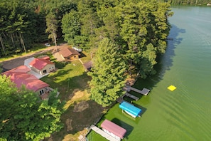 Vista aérea de uma propriedade à beira do lago, com várias cabanas, um píer e um barco pequeno.