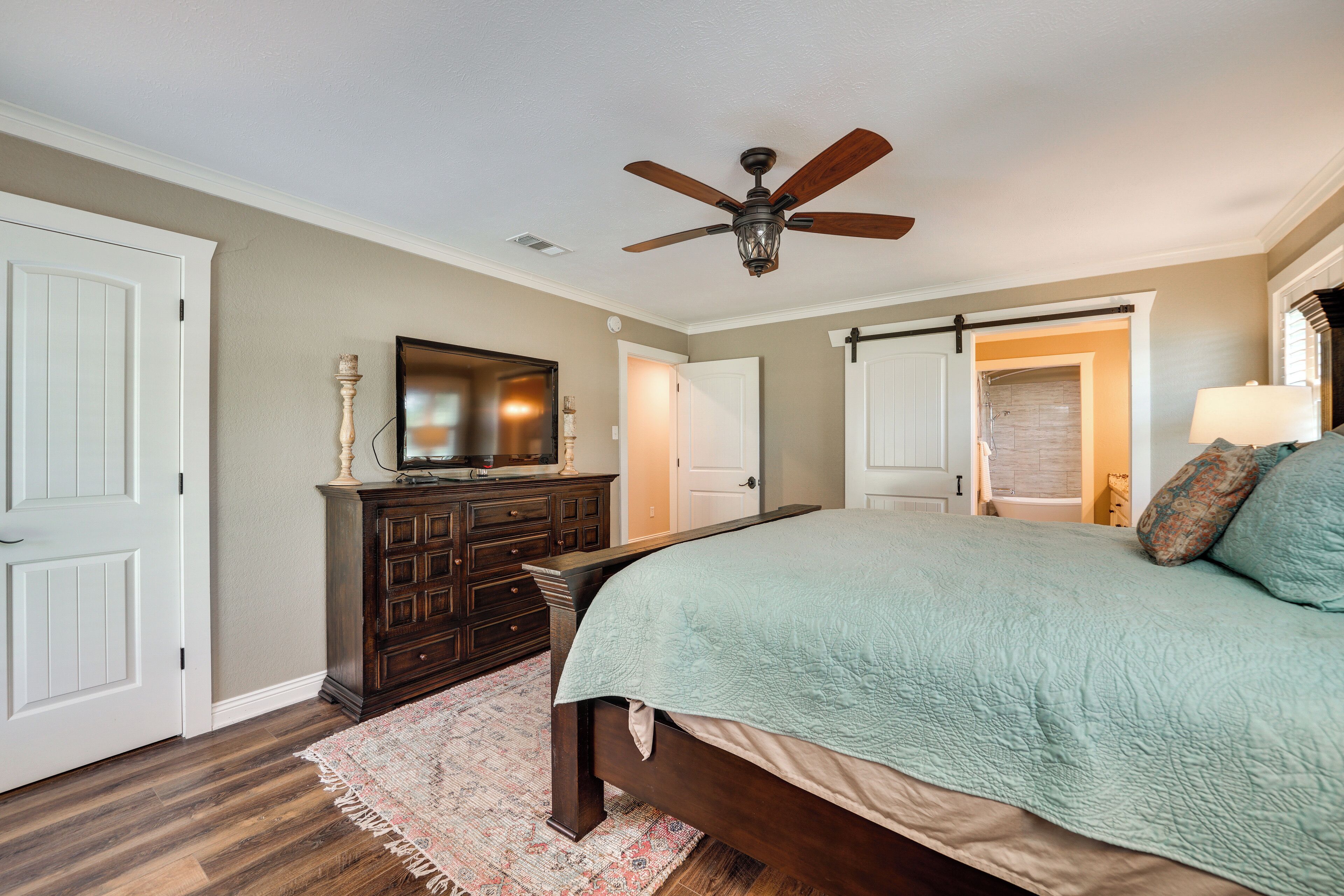 Un dormitorio con cama, cómoda, ventilador de techo y puerta que da a otra habitación.