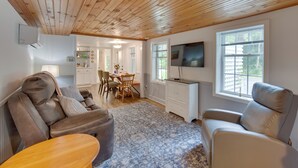 A living room with a wooden ceiling, a TV mounted on the wall, and a dining area in the background. - Charming Manheim Cottage w/ On-site Animal Viewing (Manheim)
