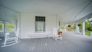 A covered porch with white railings, a bench, and a rocking chair. - Historical Magnesia Springs Home, Near Kayaking! (Cambridge Springs)