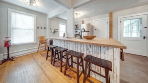 A kitchen with a wooden bar area, white walls, and a large window. - Historical Magnesia Springs Home, Near Kayaking! (Cambridge Springs)