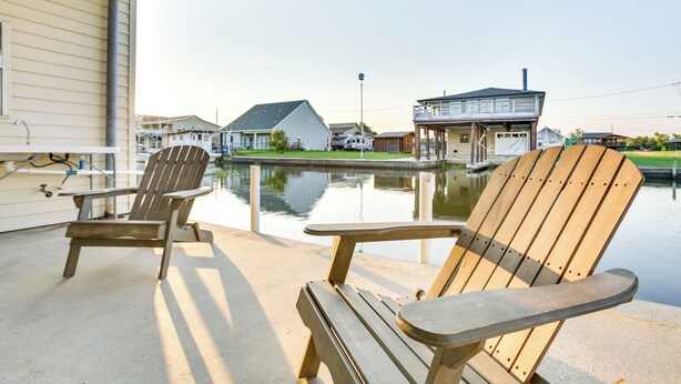 Un espace extérieur abrité, doté de deux fauteuils Adirondack et d’un sol en béton, qui offre une vue sur une étendue d’eau calme et des maisons résidentielles.