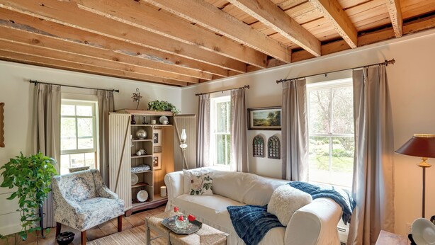 A cozy living room with a white sofa, a patterned armchair, and a wooden coffee table. A large window with curtains allows natural light to fill the space. - Mountain Biking Hub: 5 Mi to Berkshire East! (Charlemont)