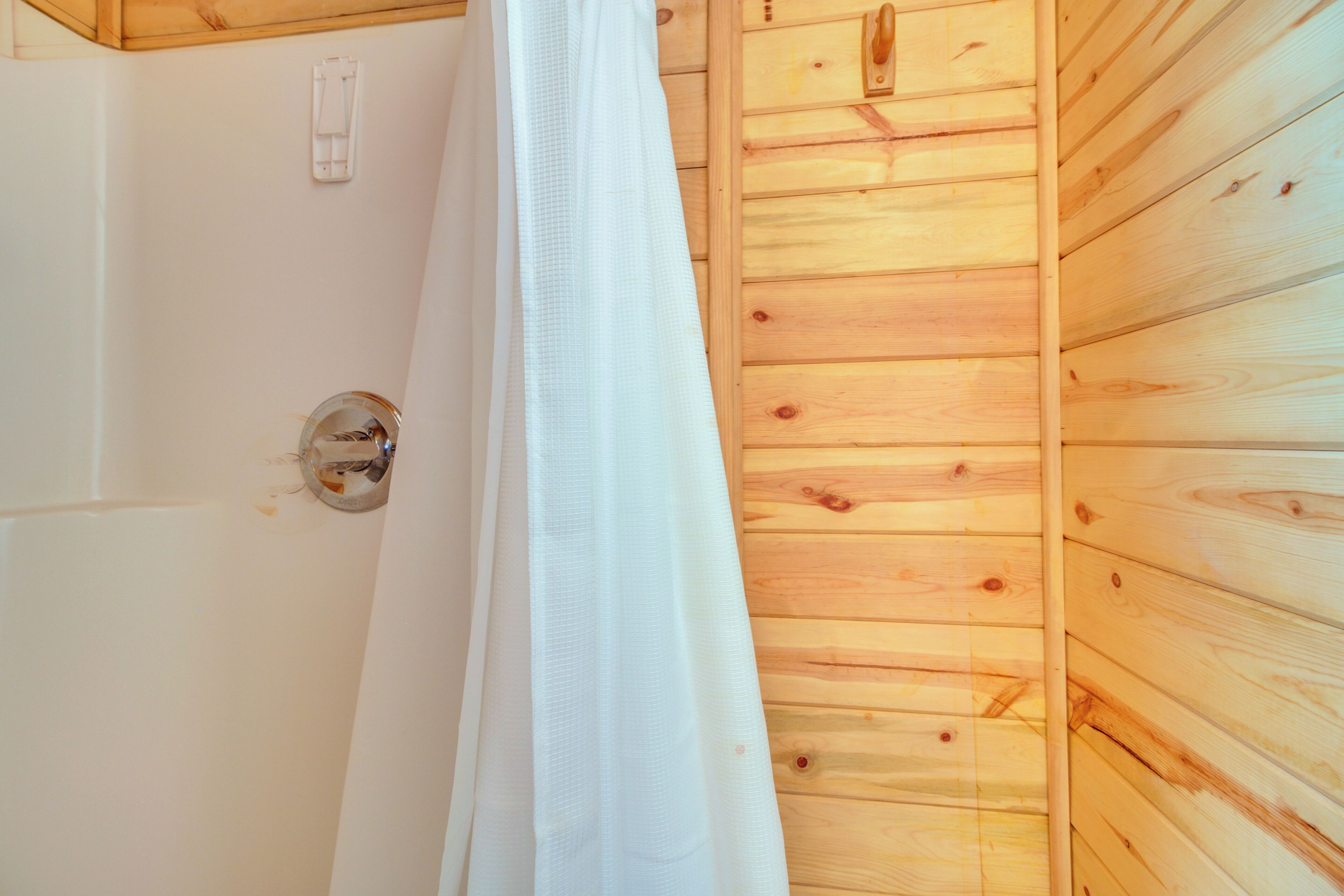 A wooden cabin interior with a shower area, a white curtain, and a visible electrical outlet.