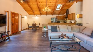Een ruime woonkamer met een houten plafond, een bank, een bijzettafeltje en een televisie.