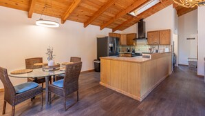 Een moderne keuken met houten kasten, een centraal eiland en een eethoek met rieten stoelen en een glazen tafel.