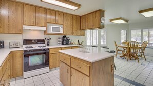 A kitchen with wooden cabinets, a white countertop, a stove, a microwave, and a dining area with chairs and a table. - Charming Elko Home w/ Pool Table! (Elko)