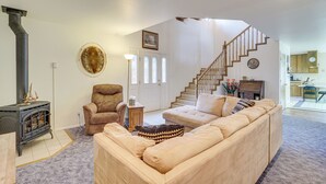 A living room with a fireplace, a sofa, a chair, and a staircase leading to an upper level. - Charming Elko Home w/ Pool Table! (Elko)