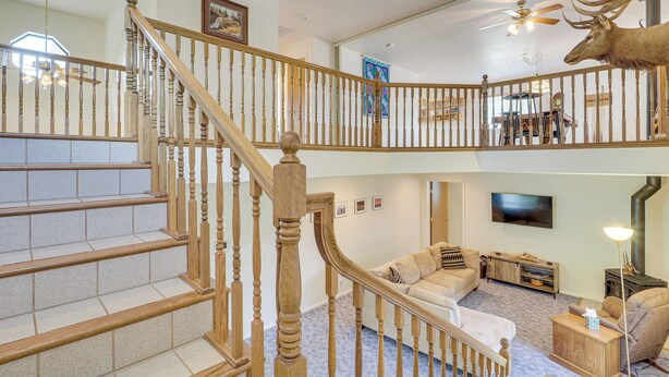 A two-story home with a wooden staircase, a living room with a sofa and a television, and a deer head decoration on the upper floor. - Charming Elko Home w/ Pool Table! (Elko)