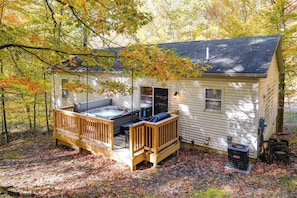 A cabin with a hot tub, deck, and outdoor seating area surrounded by trees.