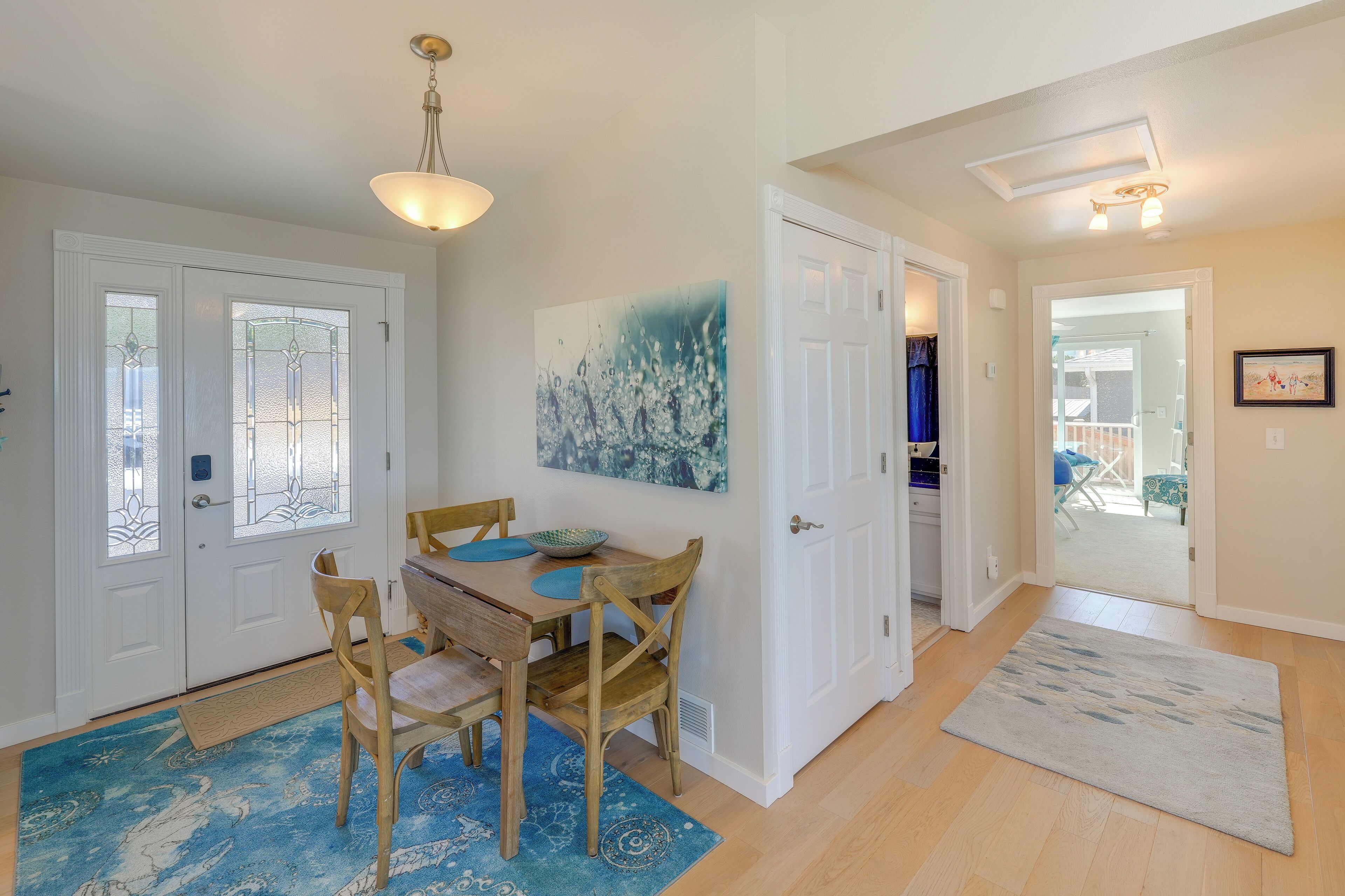 A dining area with a wooden table and chairs, a blue rug, and a painting on the wall.
