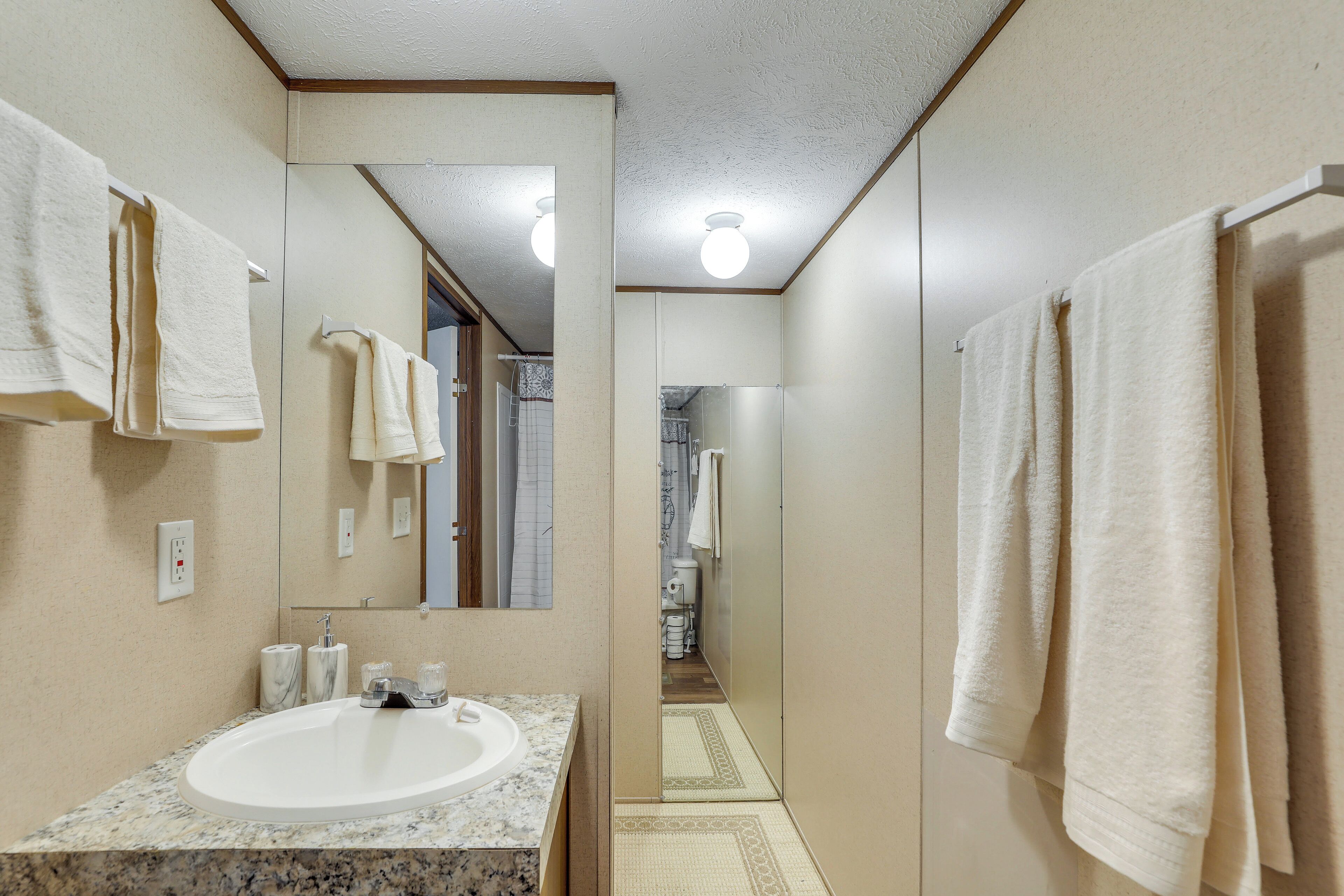 Un baño con lavamanos, espejo, toallas y ducha.