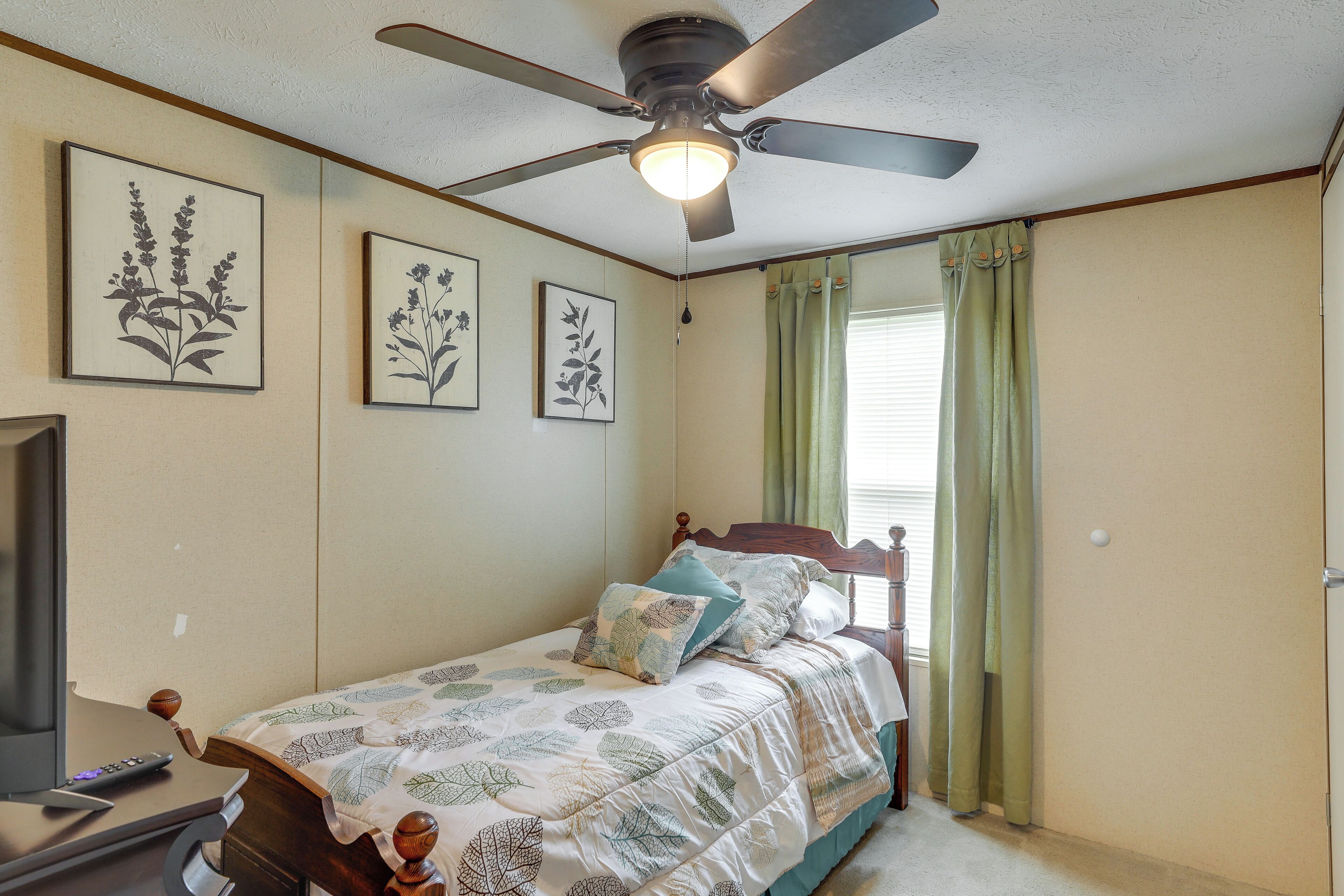A bedroom with a bed, a ceiling fan, and framed botanical prints on the wall.