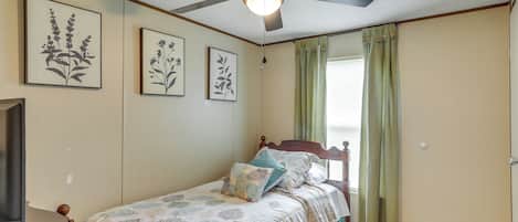 A bedroom with a bed, a ceiling fan, and framed botanical prints on the wall.