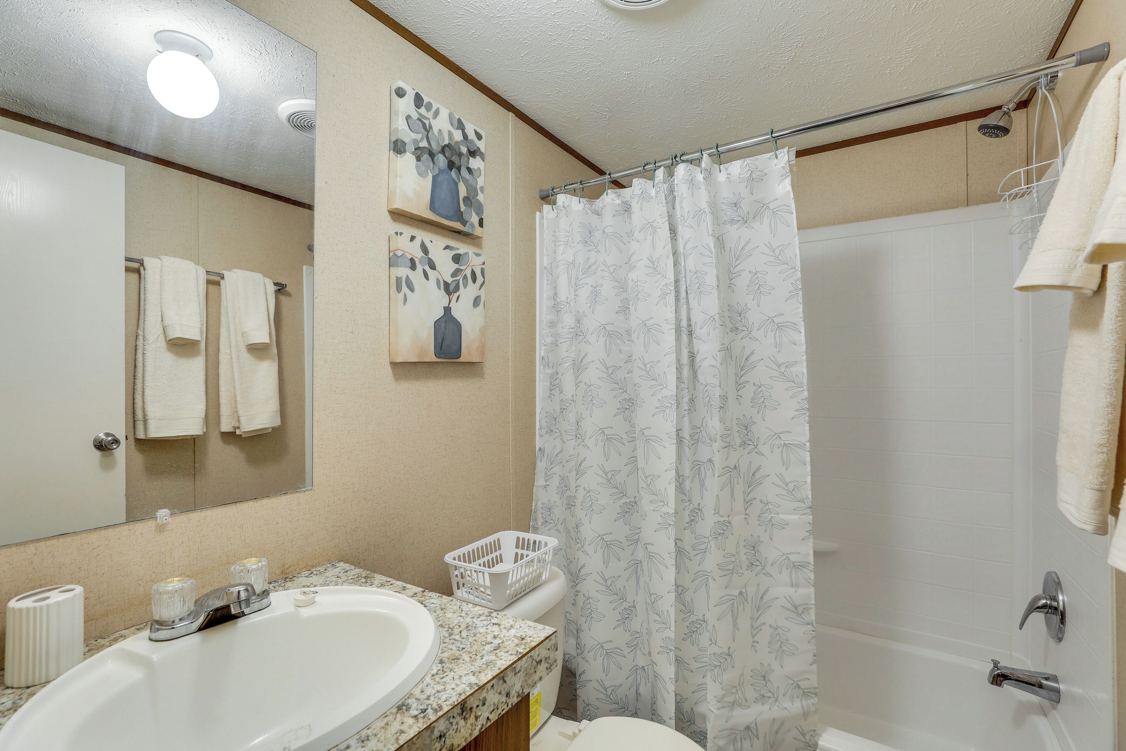 A bathroom with a sink, mirror, shower curtain, and towels.