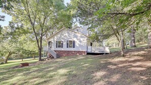 A white house with a porch, surrounded by trees and a sloped lawn. - Peaceful Pineville Vacation Rental w/ Grill! (Pineville)