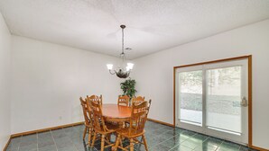 A dining room with a round wooden table and chairs, a chandelier, and a sliding glass door. - Peaceful Pineville Vacation Rental w/ Grill! (Pineville)