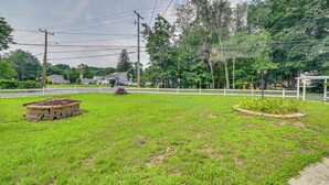 A grassy area with a small stone structure, a white fence, and trees in the background. - East Hartford Studio ~ 4 Mi to Downtown Hartford! (East Hartford)
