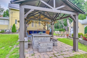 A covered outdoor patio with a stone bar and seating area, surrounded by a brick pathway and a grassy lawn.