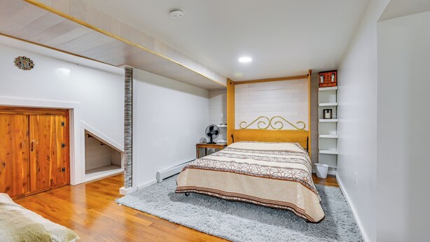 A bedroom with a wooden bed, a small bedside table, a fan, and a shelf with books. - East Hartford Studio ~ 4 Mi to Downtown Hartford! (East Hartford)