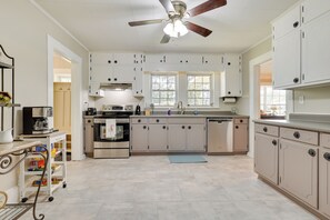 A kitchen with white cabinets, a ceiling fan, and a window.