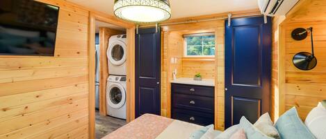 A wooden cabin bedroom with a bed, pillows, a washing machine, and a small window.