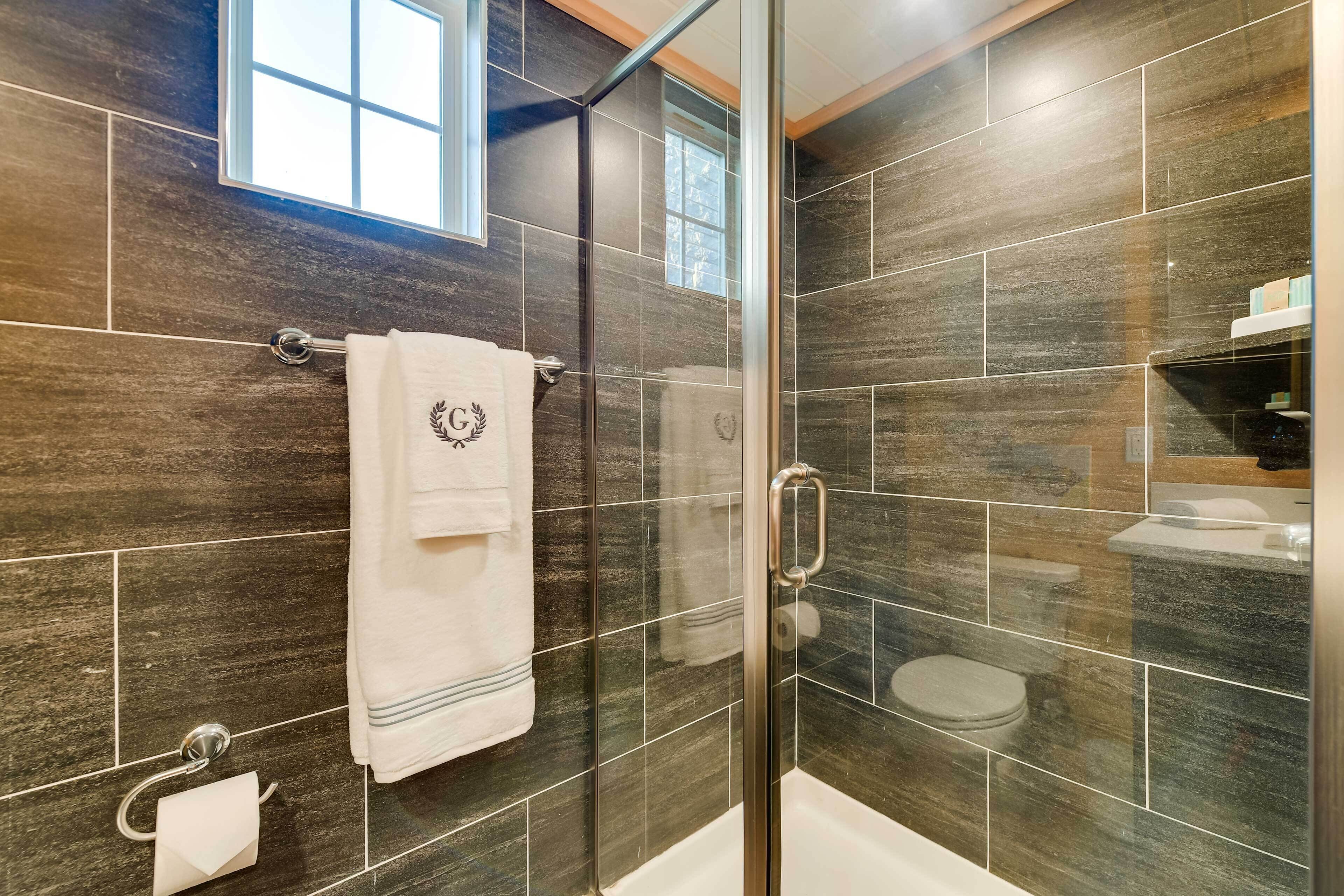 A modern bathroom with dark tiles, a glass shower enclosure, a white towel, and a visible toilet.