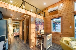 Interior de una cabaña con revestimiento de madera, un dormitorio en altillo, una zona de comedor y una ventana con vistas.