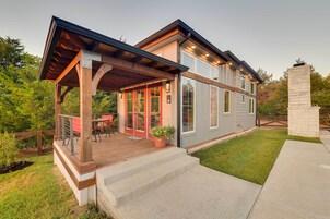 Una casa moderna de dos pisos con terraza de madera, un patio cubierto y una chimenea de piedra.