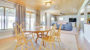 Un vaste espace de vie doté d’un plafond en bois, d’une table à manger ronde entourée de chaises et d’un canapé placé au fond de la pièce.