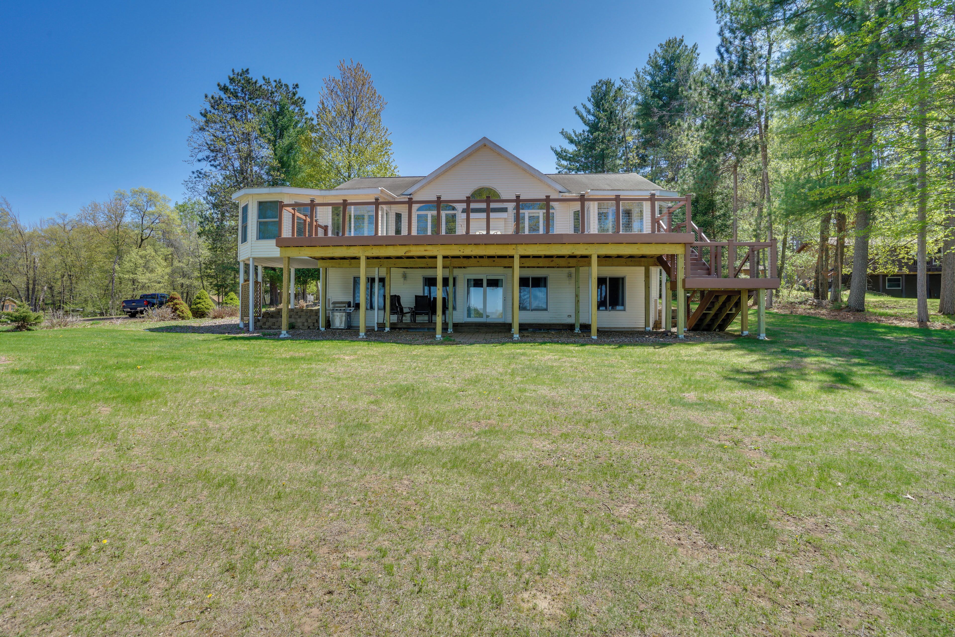 A two-story house with a covered porch and a deck, surrounded by a grassy yard and trees.