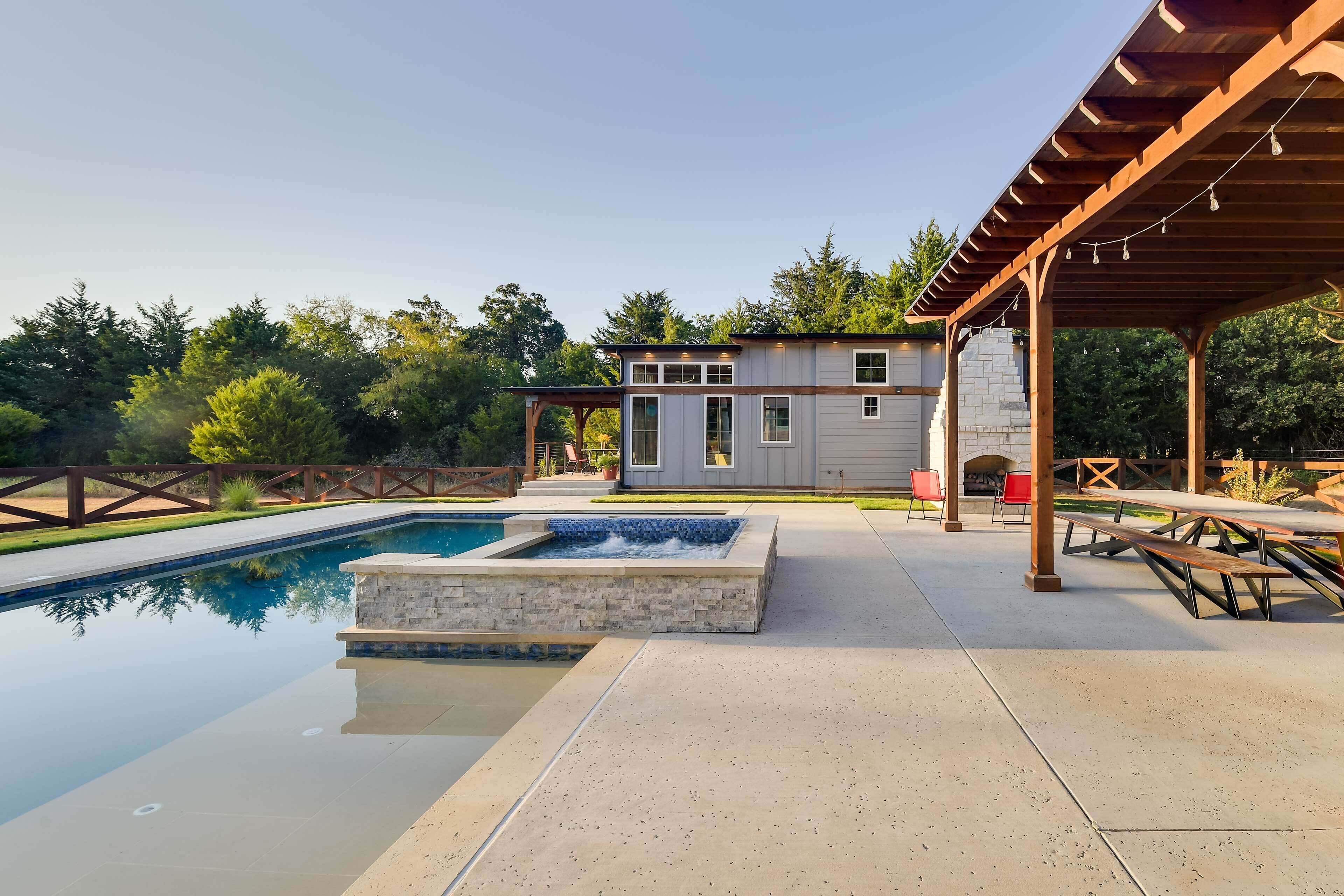 Una piscina con detalles de piedra, un patio cubierto y un pequeño edificio con chimenea.