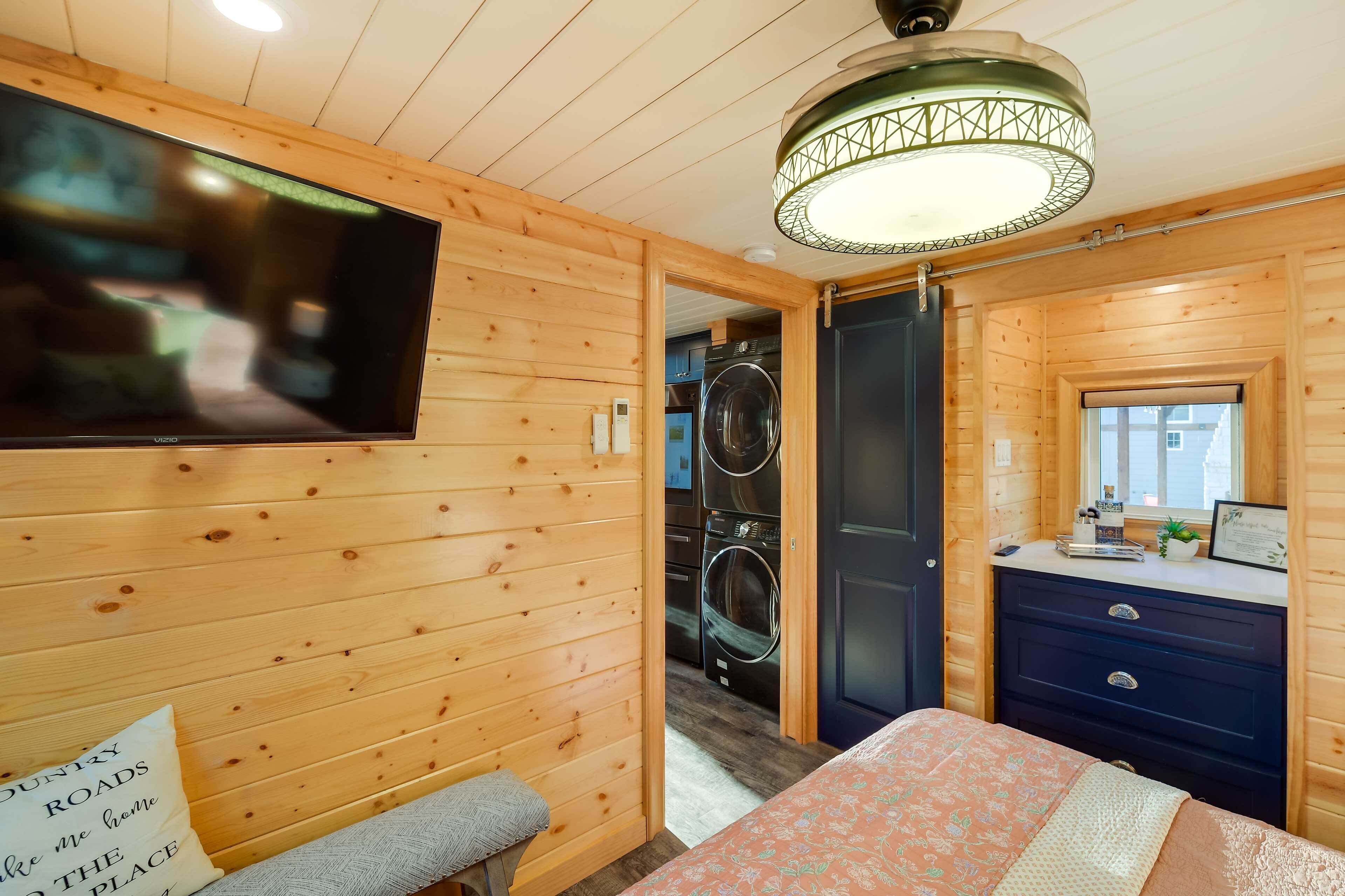 Una habitación de madera con una cama, un banco, un televisor, una lavadora y un aparador.