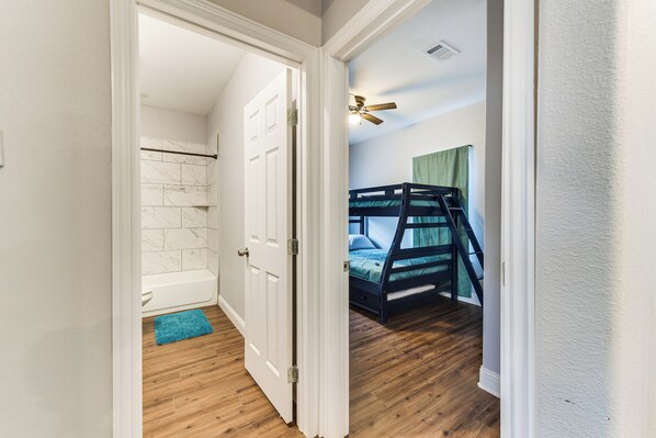 A bedroom with a bunk bed, a bathroom with a bathtub, and a wooden floor. - Texas Family Home w/ Hot Tub: 1 Mi to Lake Whitney (Whitney)