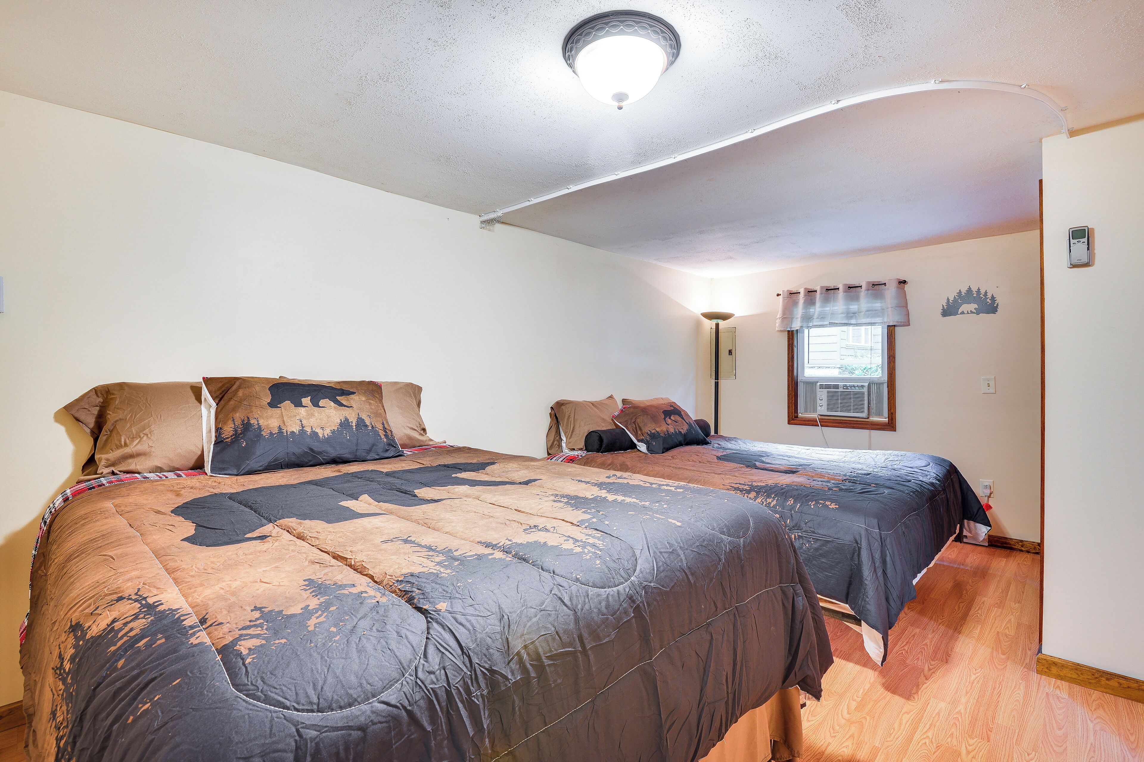A bedroom with two beds, a ceiling light, a window with curtains, and a wall-mounted air conditioning unit.