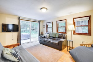 Una habitación acogedora con sofá de cuero, un televisor de pantalla plana, una lámpara y vistas al exterior a través de amplios ventanales.
