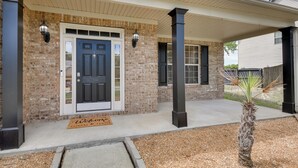 A brick house with a dark front door, a welcome mat, and a small palm tree in the front yard.