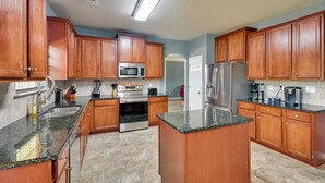A kitchen with wooden cabinets, granite countertops, stainless steel appliances, and a tiled floor.