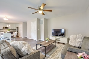 Ein modernes Wohnzimmer mit Sofa, Couchtisch und Fernseher. Im Hintergrund sind ein Deckenventilator und eine Küche zu sehen.