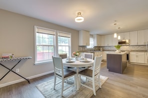 A modern kitchen with white cabinets, a central island, and a dining area with a round table and chairs.