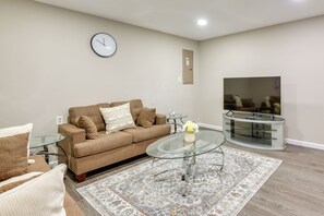 A living room with a brown sofa, a glass coffee table, a TV on a stand, and a patterned rug.