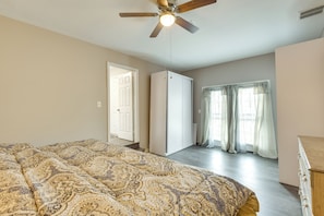 A bedroom with a bed, a ceiling fan, a wardrobe, and a window with curtains.