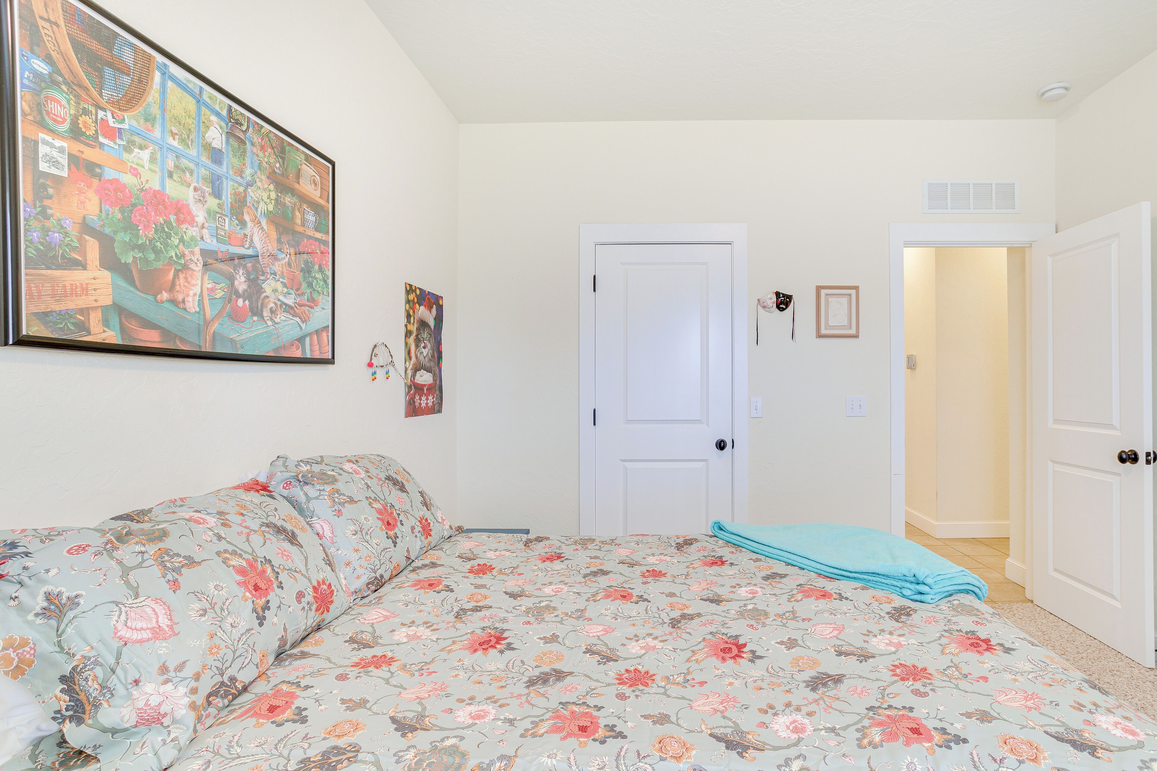 Ein Schlafzimmer mit einem blumigen Bettüberwurf, einem großen Gemälde an der Wand und einer Tür zu einem anderen Raum.
